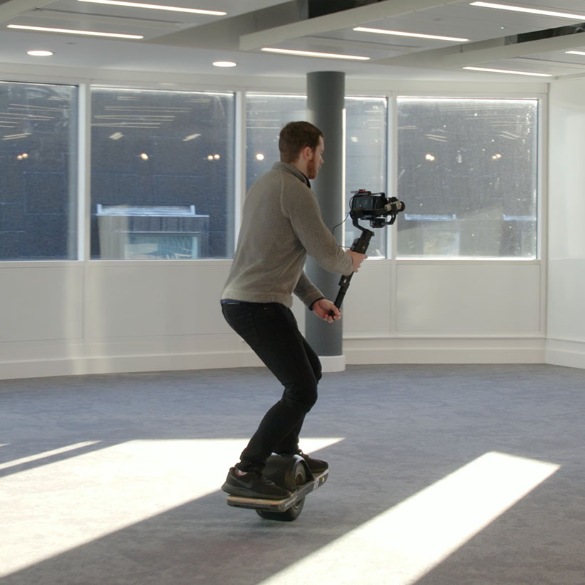 Videographer doing video production rides a onewheel while filming inside a building