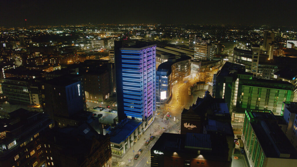 A photo of the 111 Piccadilly building taken at night. It's lit up by blue lights